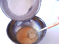 混ぜ合わせたバターと砂糖と卵の中に、ふるった米粉等を入れている写真